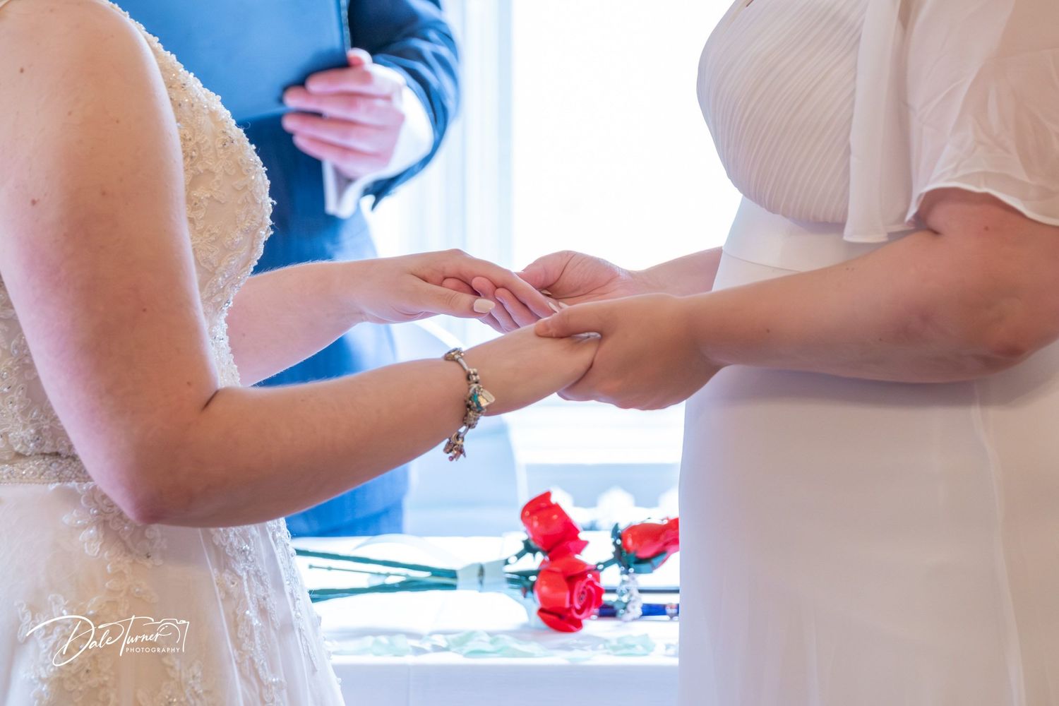 Wedding ceremony participants exchanging rings with red floral accents visible.