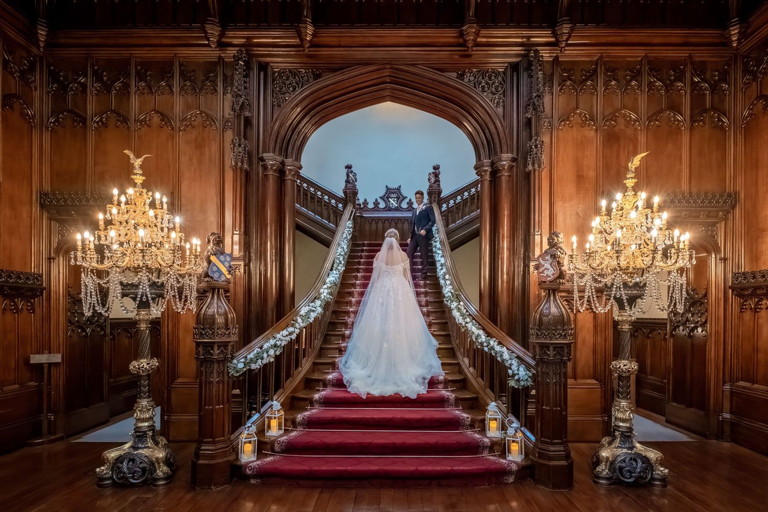Elegant wood-paneled great hall with crystal chandeliers and red carpet leading to ornate altar.