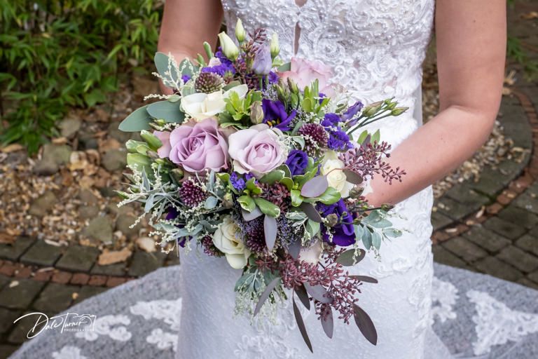 Close-up details of purple and pink wedding bouquet with delicate lace dress.