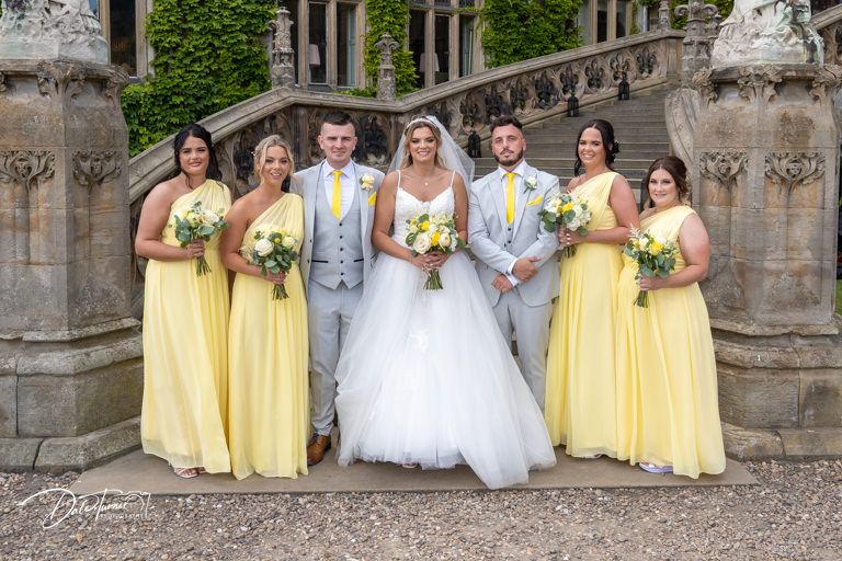 Wedding party in yellow dresses and white gown posing on stone steps.