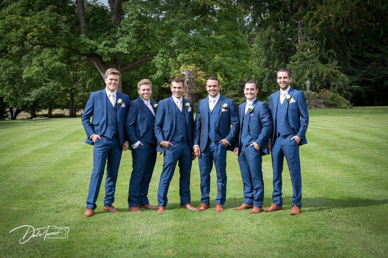 Groomsmen in matching blue suits pose on manicured lawn.