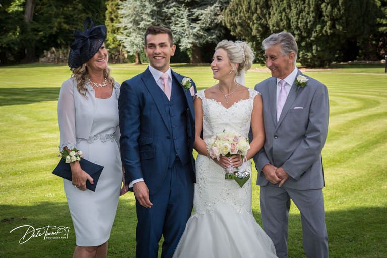 Wedding party poses for formal portraits on expansive green lawn.