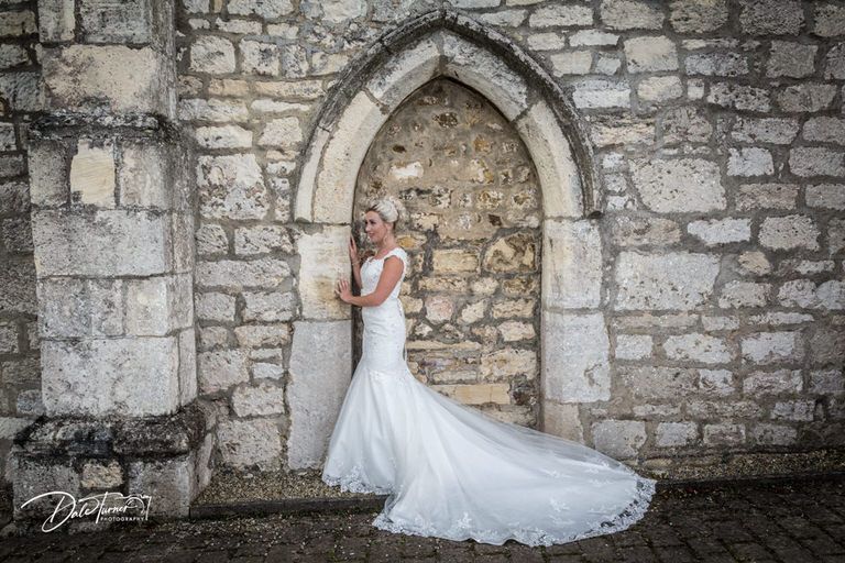 Stone wall backdrop with gothic archways creates dramatic setting for bridal portraits.