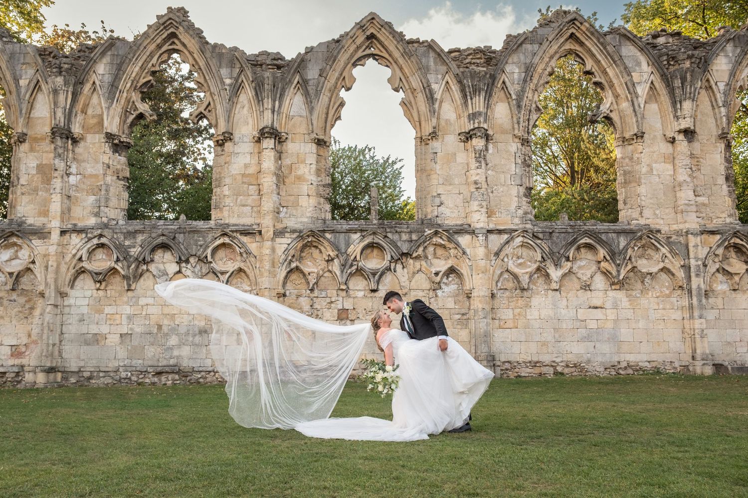 Elegant wedding photo captured against ancient stone abbey ruins with flowing veil.