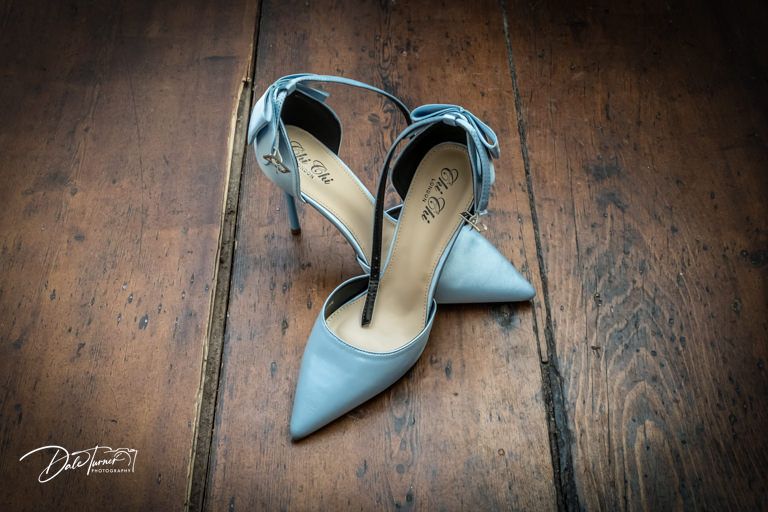 Light blue wedding shoes photographed on rustic wooden flooring.