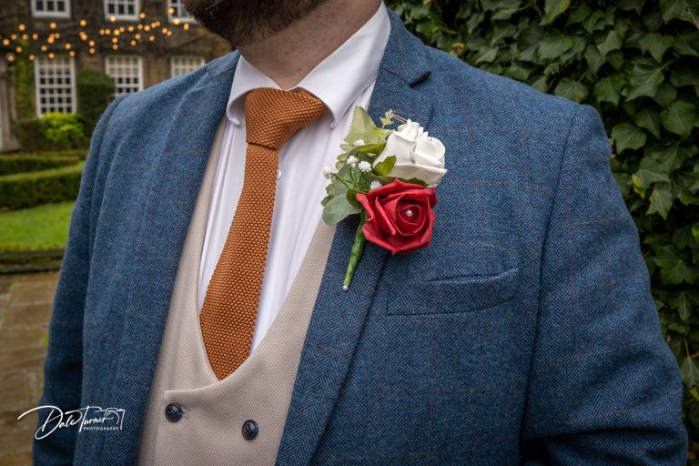 Close-up details of navy blue suits with red boutonnieres and brown leather accessories.
