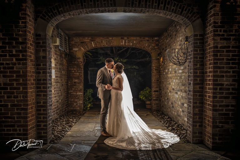A romantic wedding portrait of a couple in a rustic brick tunnel with flowing veil.