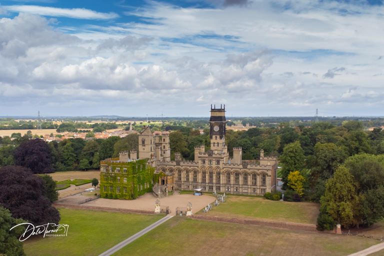 Aerial panoramic view of a stately manor house surrounded by manicured lawns and gardens.