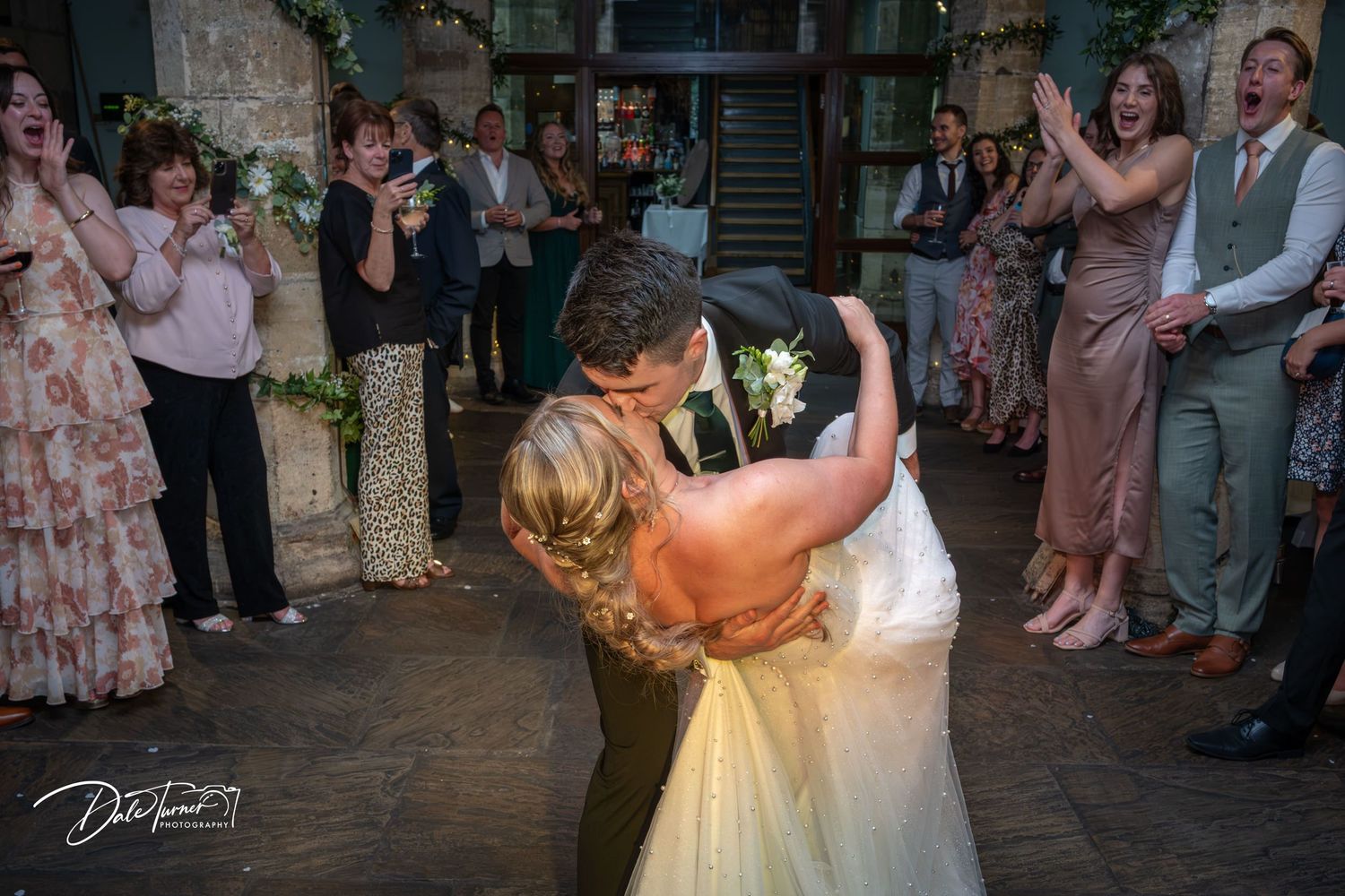 A romantic first dance moment captured at a rustic indoor wedding venue with guests watching.