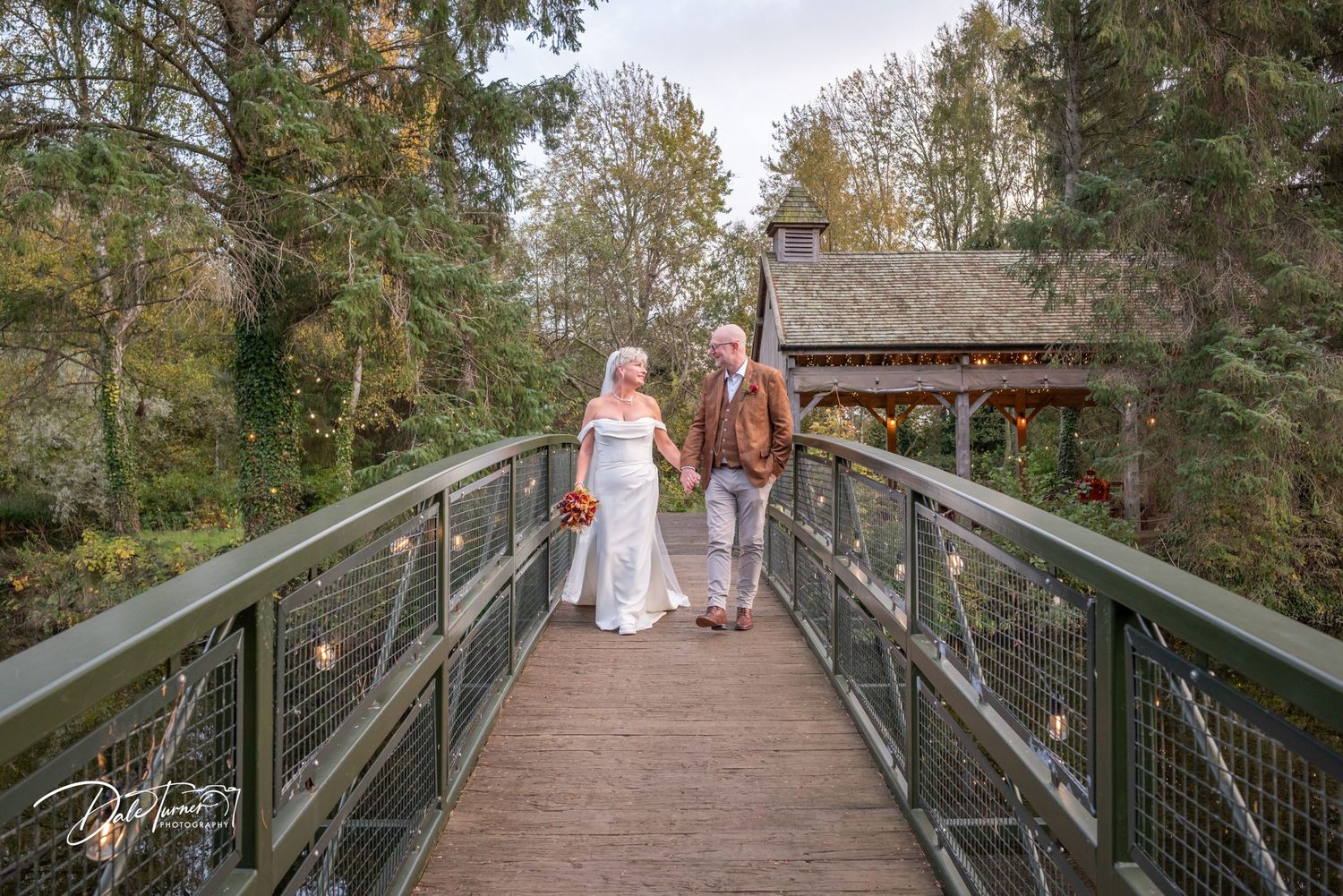 Wooden bridge walkway surrounded by autumn trees in a scenic outdoor setting.