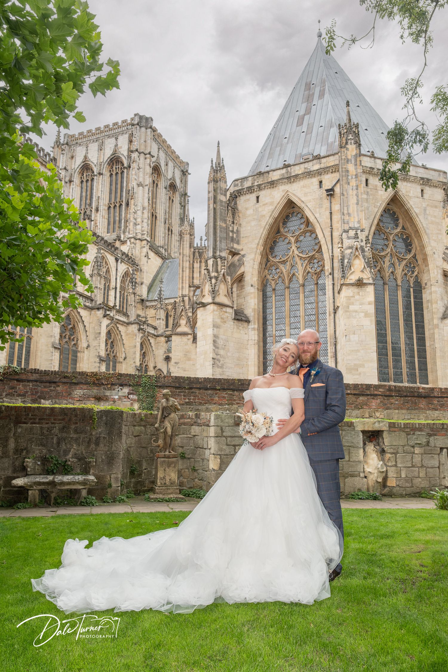 Bride and groom pose romantically in front of York Minster Cathedral on their wedding day.