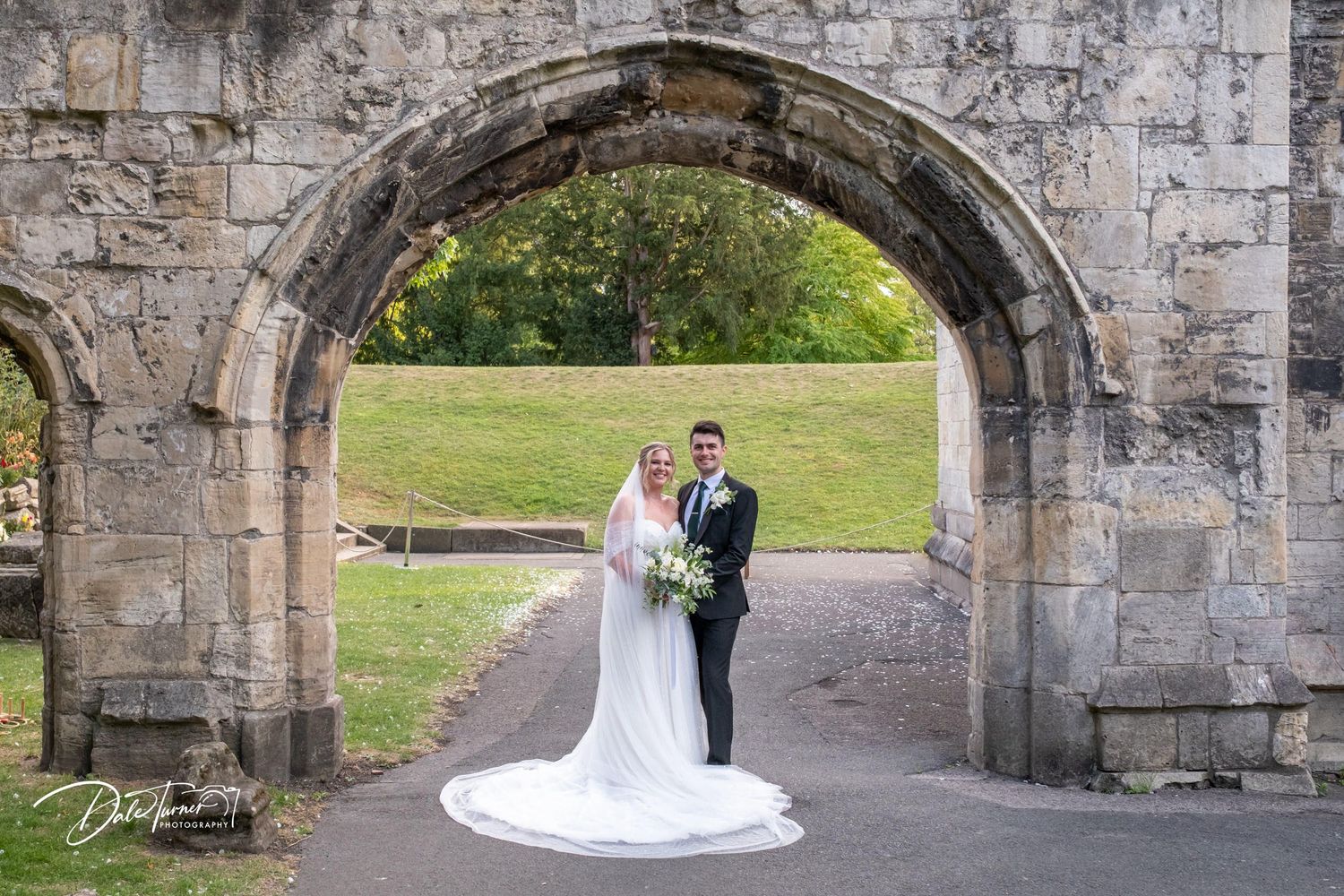 Romantic wedding photos under historic stone archways with flowing white dress train.