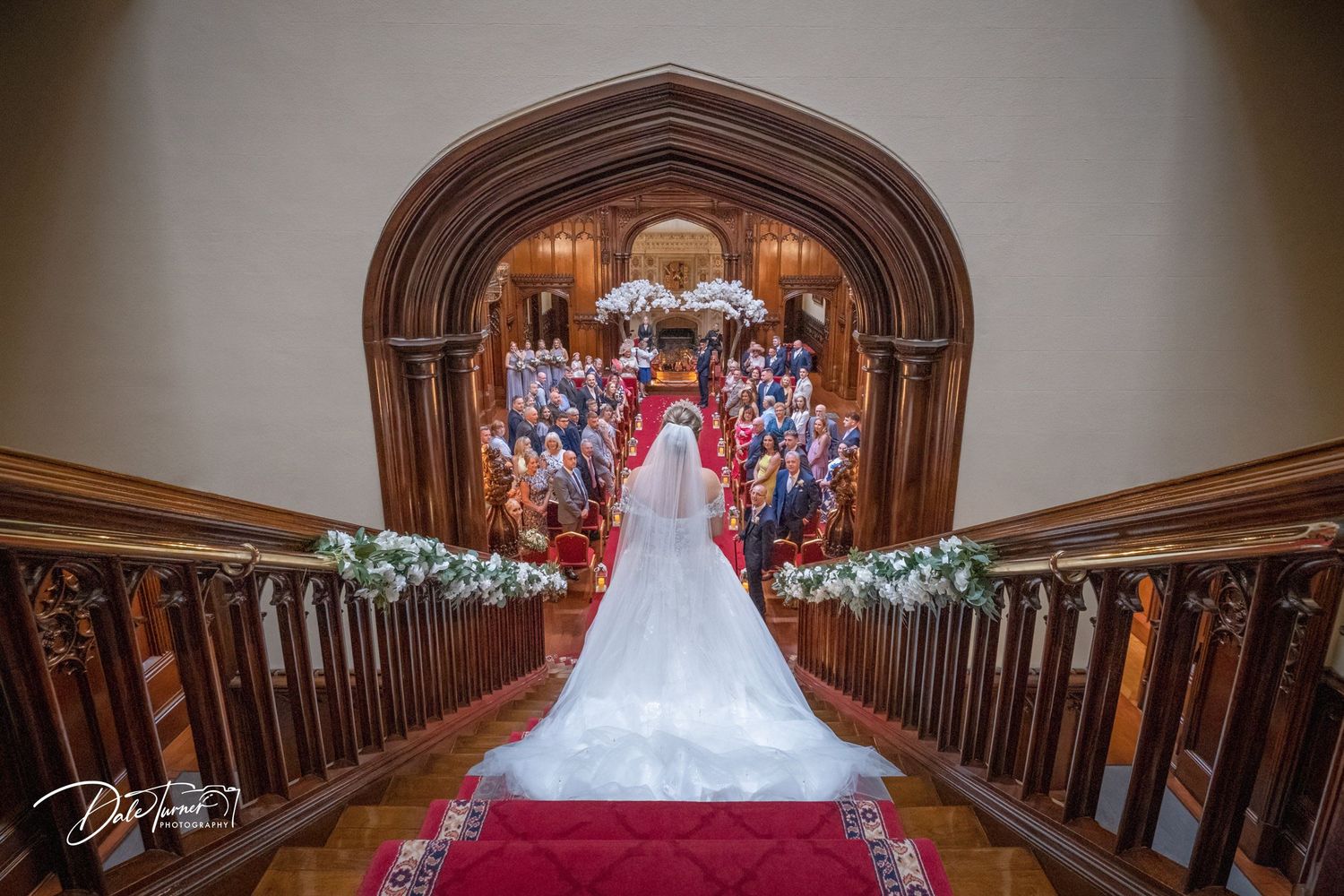 Elegant wedding venue interior with grand wooden staircase and ornate chandeliers.