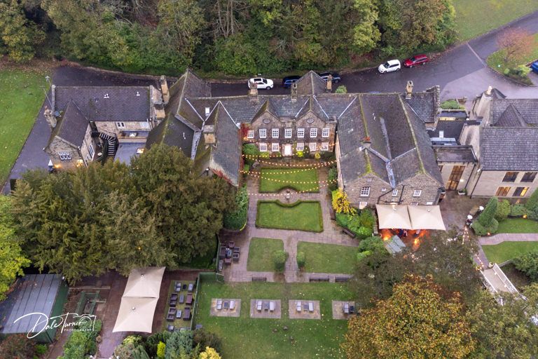 Aerial view of a grand stone manor house and surrounding gardens on wedding day.