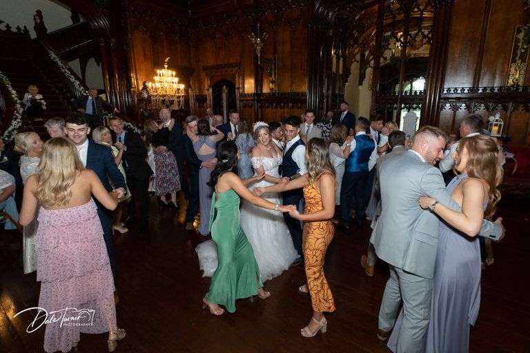 Wedding reception dance floor filled with guests celebrating in dimly lit venue.