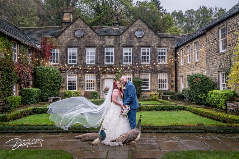 Wedding couple photographed in front of a historic stone mansion with elegant landscaping and architecture.
