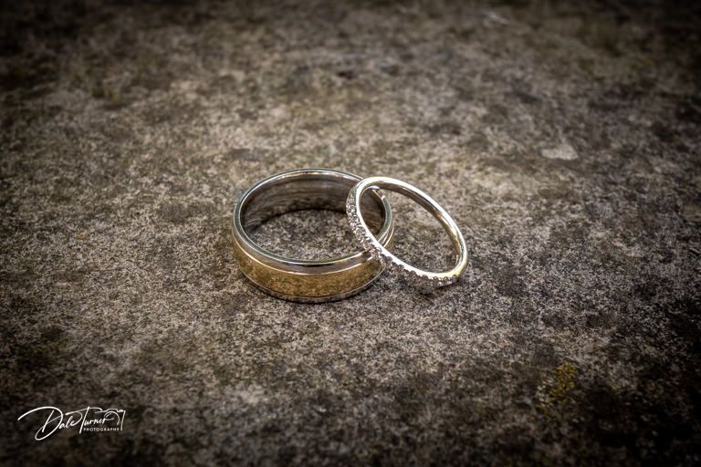 Wedding rings photographed on textured dark background with dramatic lighting.