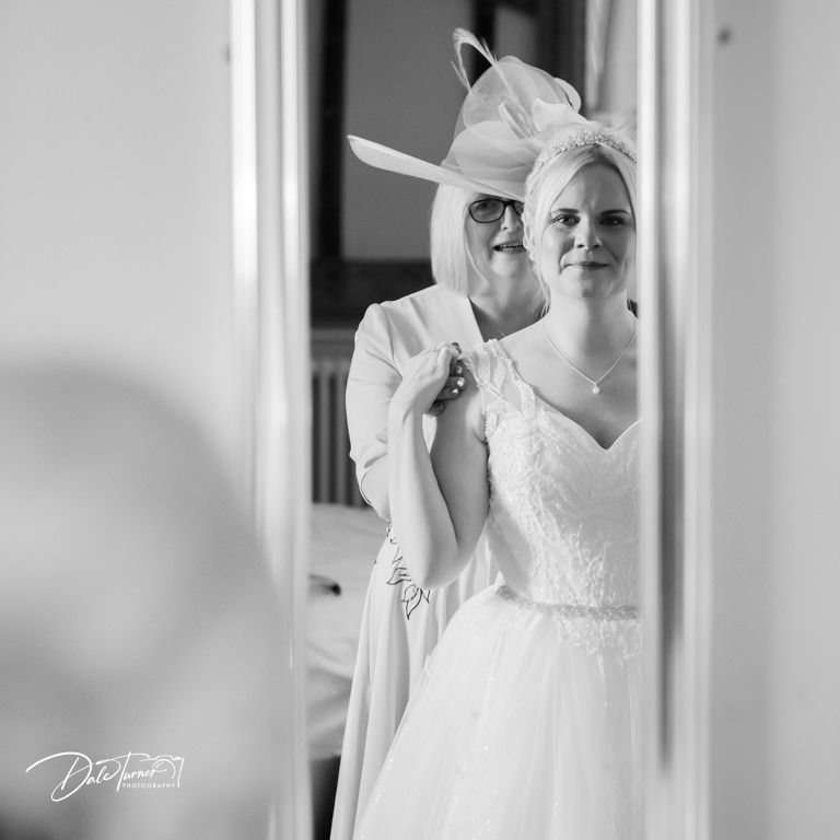 A bride in a white dress gets ready in a bright room with natural lighting.