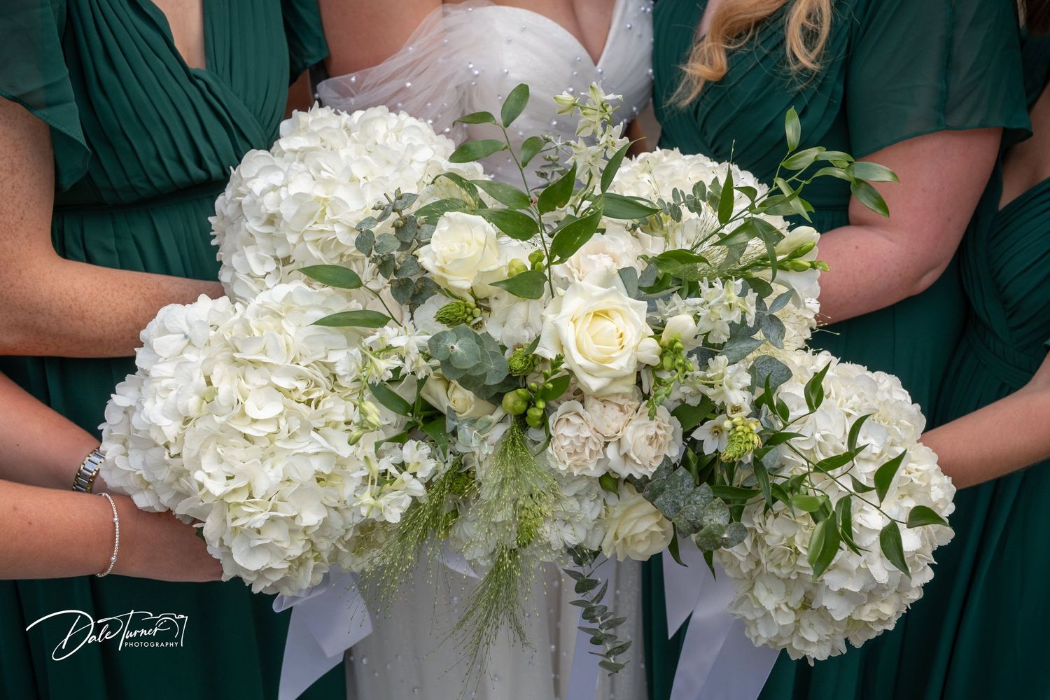 Row of elegant white and green bouquets held by bridesmaids in emerald dresses.