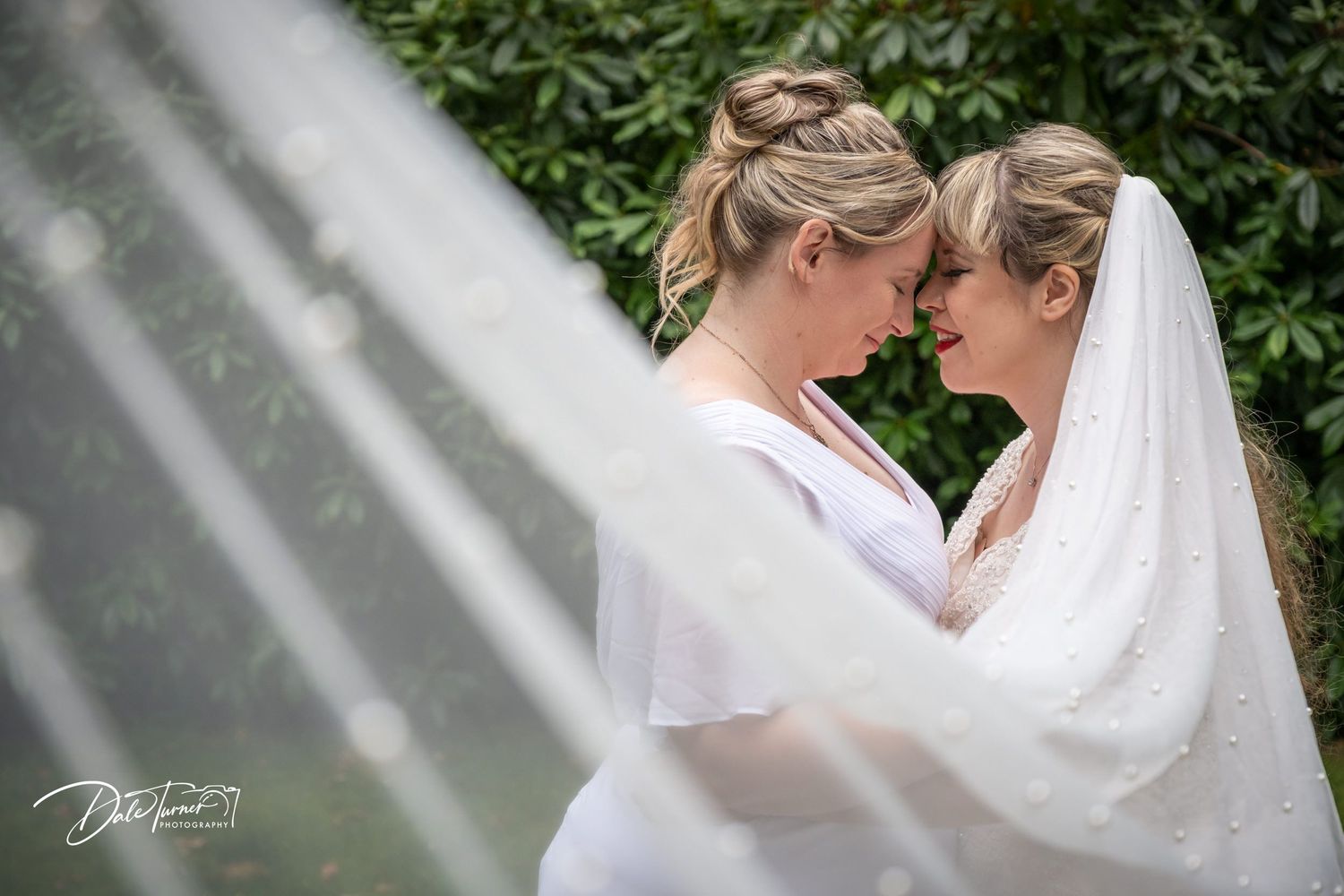 Intimate wedding portrait through a veil with green foliage background.