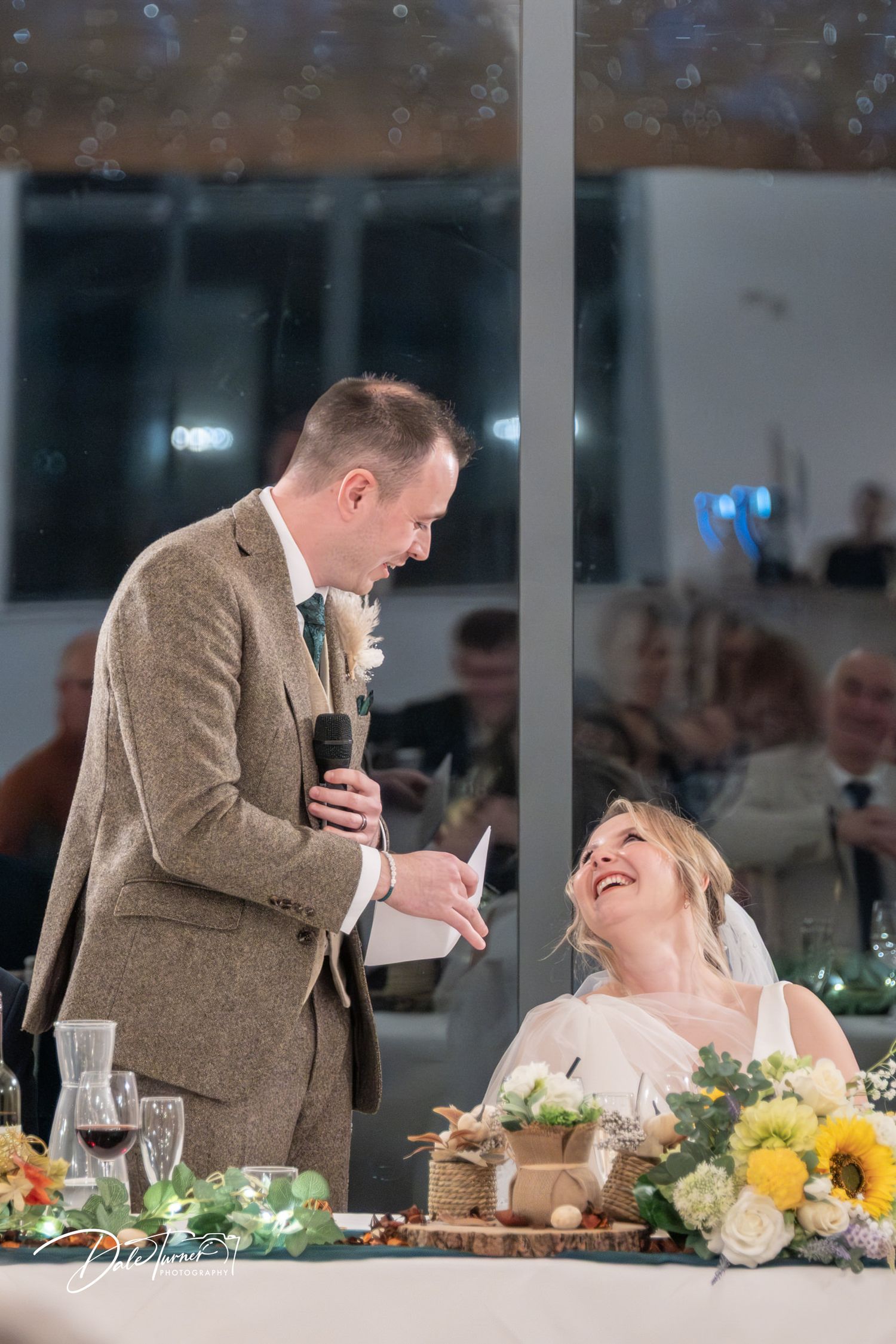 A couple shares a joyful moment at their wedding reception with yellow floral centerpieces decorating the table.