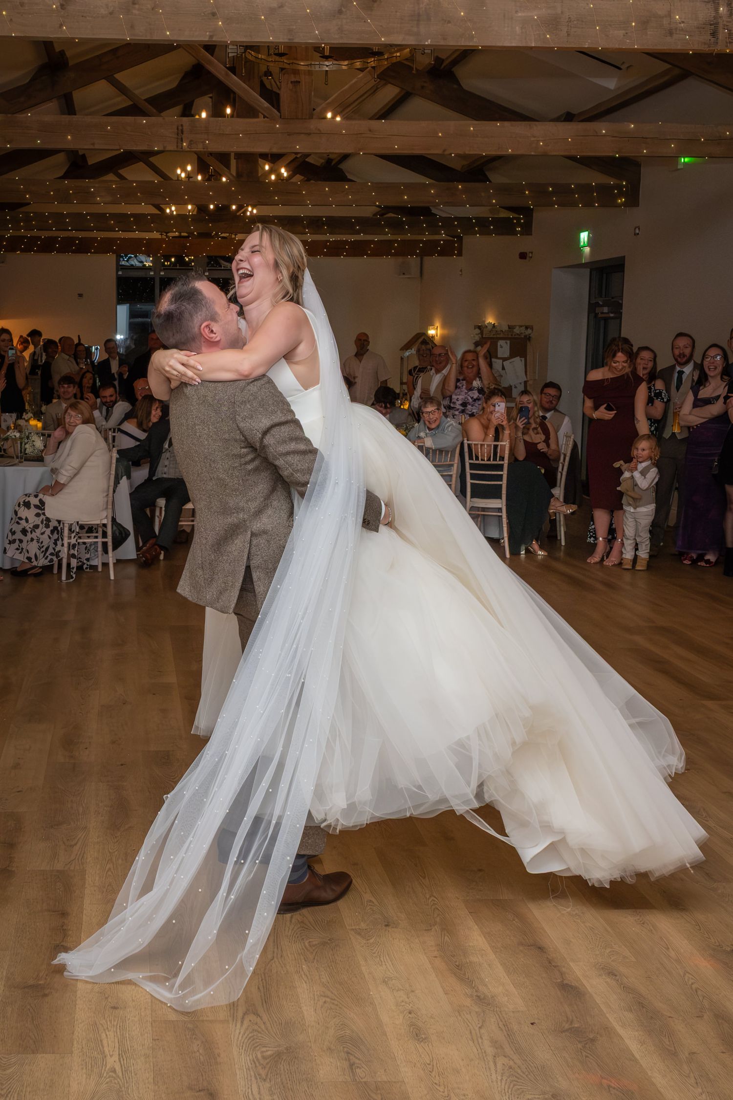 A couple performs their first dance at a wedding reception on a wooden dance floor as guests watch from the sides.