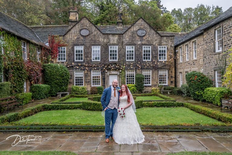 Newlyweds taking photos outside a grand stone manor house on a rainy day.