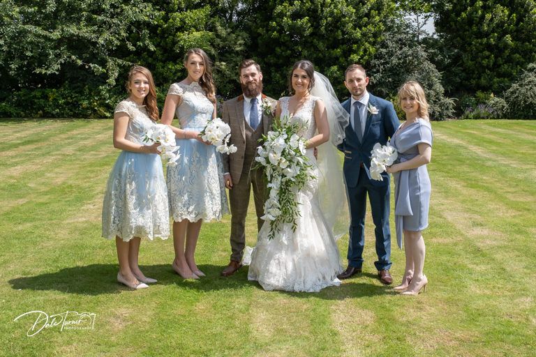 Wedding party poses together on a sunny lawn with bridesmaids in light blue dresses.