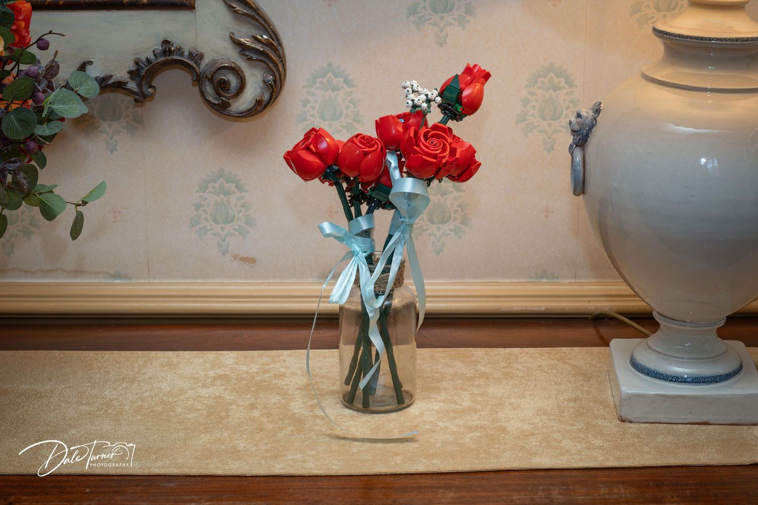 Red roses in a clear glass vase displayed on a table with decorative wall background.