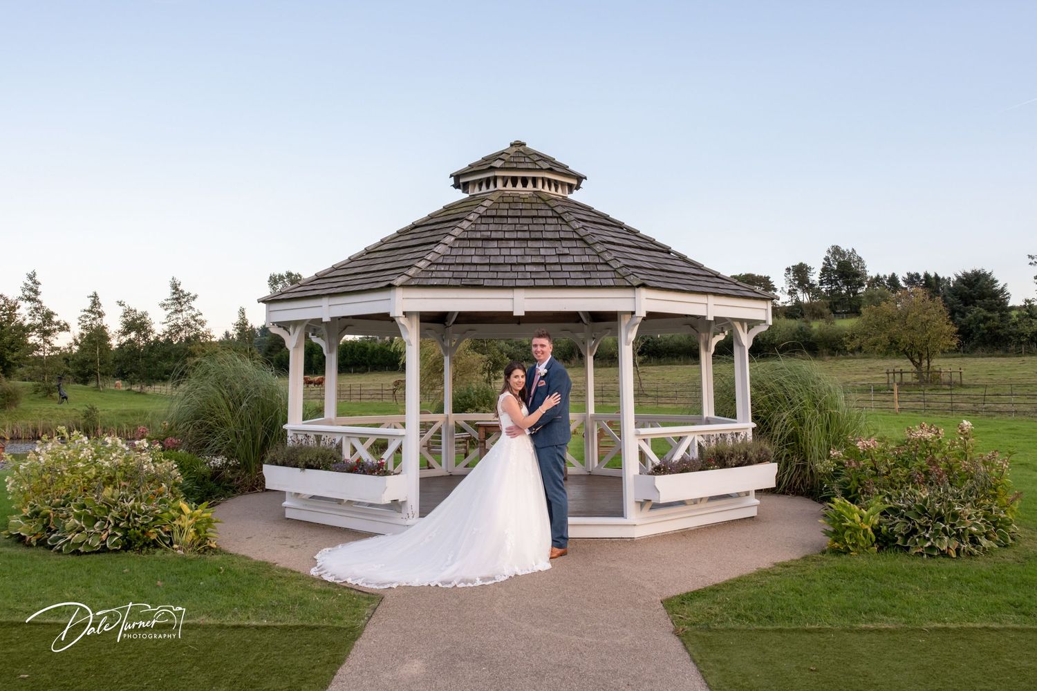 Wedding portraits taken at a classic white gazebo surrounded by manicured gardens.