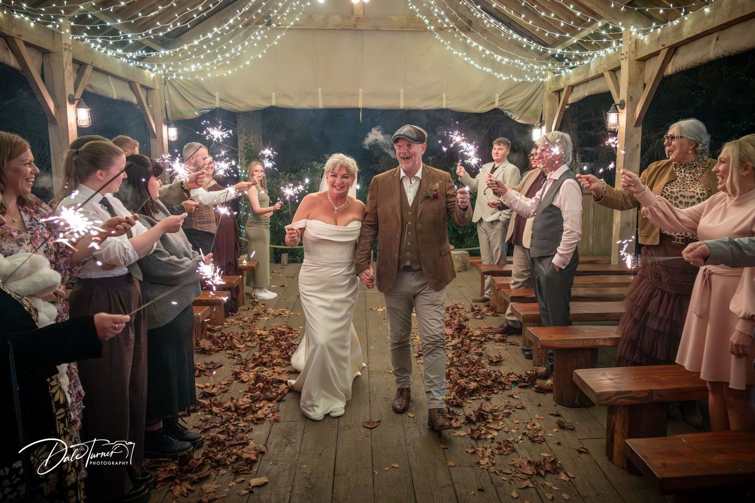 Indoor wedding venue with twinkling string lights and rustic wooden benches arranged for ceremony.
