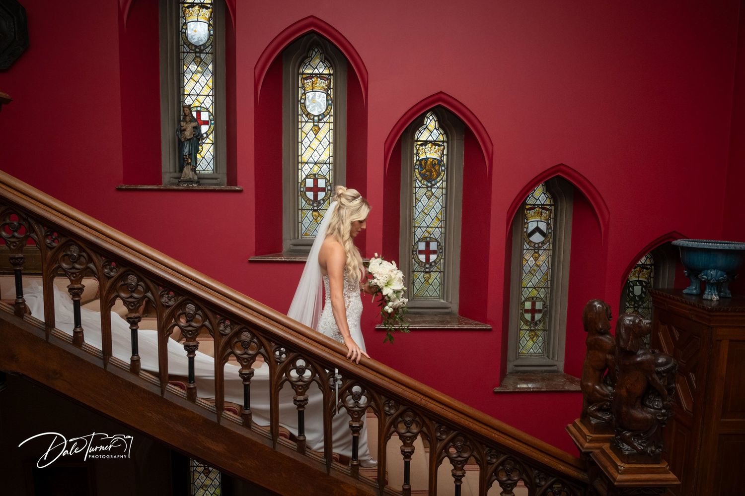 Elegant red staircase with gothic windows creates dramatic wedding venue atmosphere.
