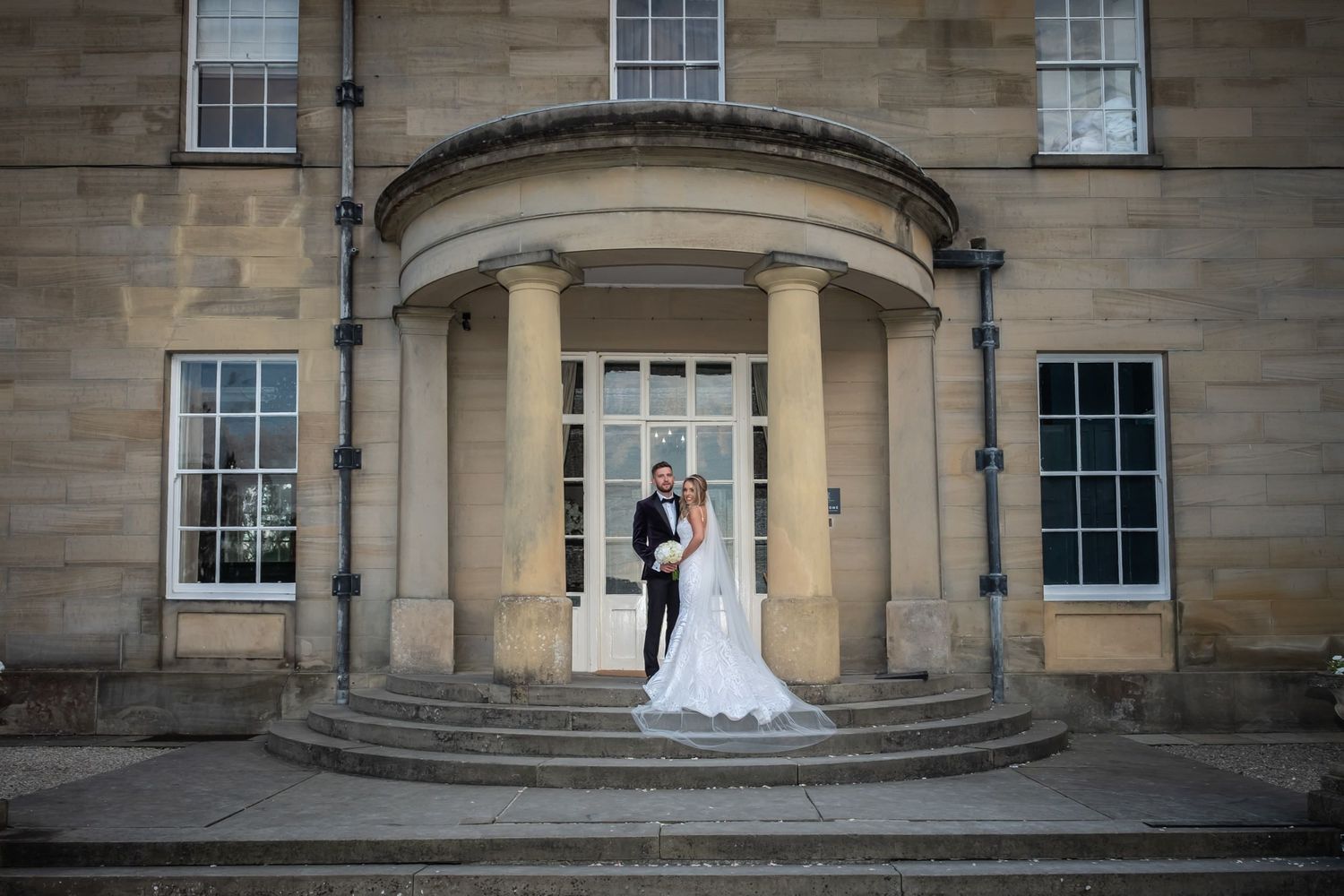 Panoramic wedding photos at a grand stone building entrance with classical columns.
