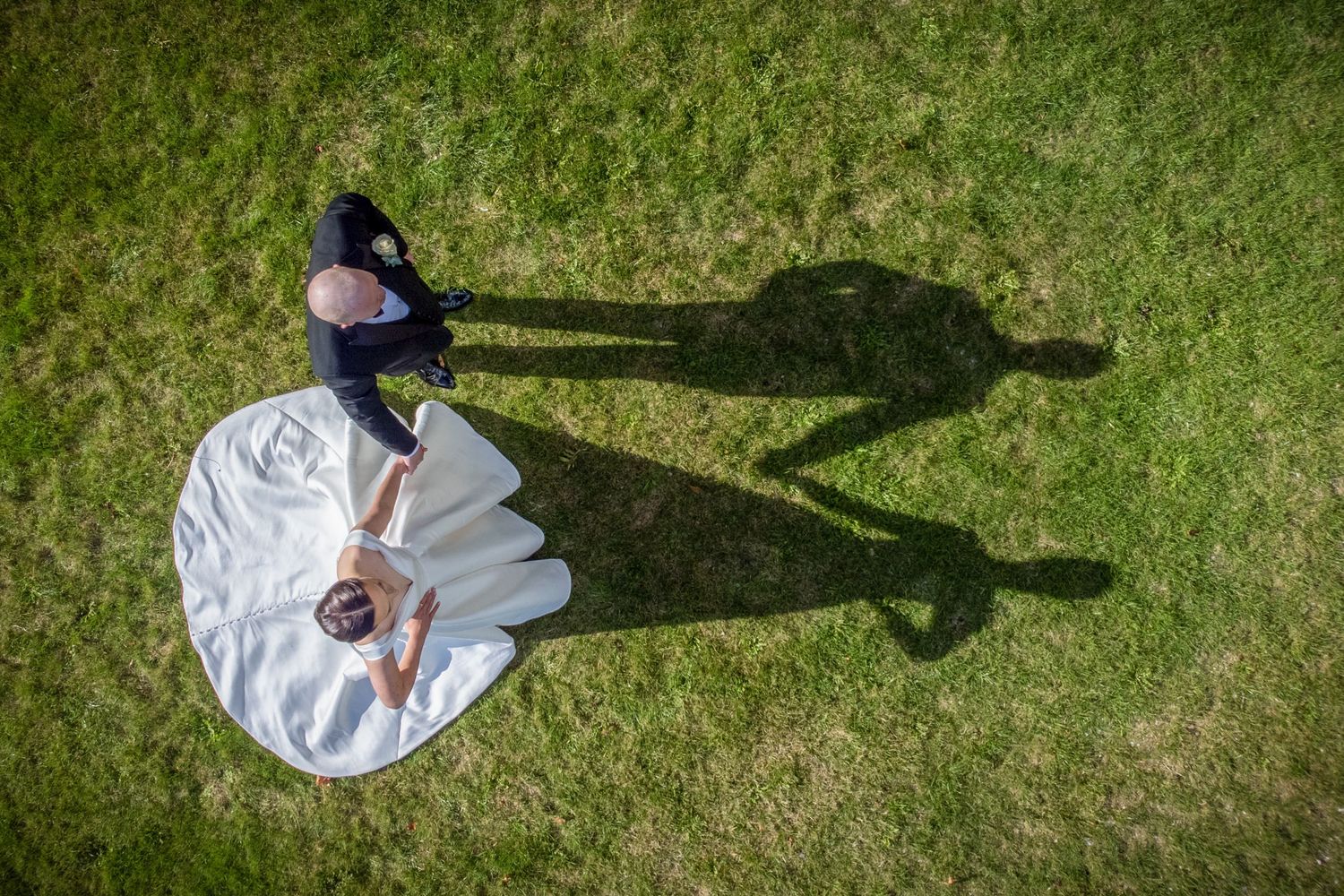 Overhead view of a couple in wedding attire creating shadows on green grass.