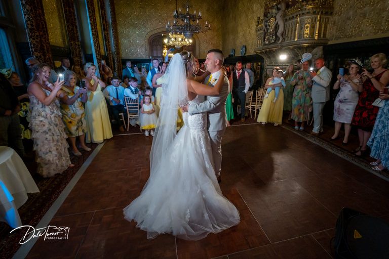 Elegant ballroom wedding reception with dancing couple surrounded by watching guests.