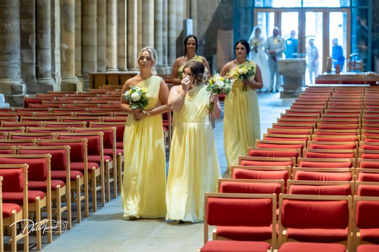 Wedding party in yellow dresses walking through church aisle with red seating.