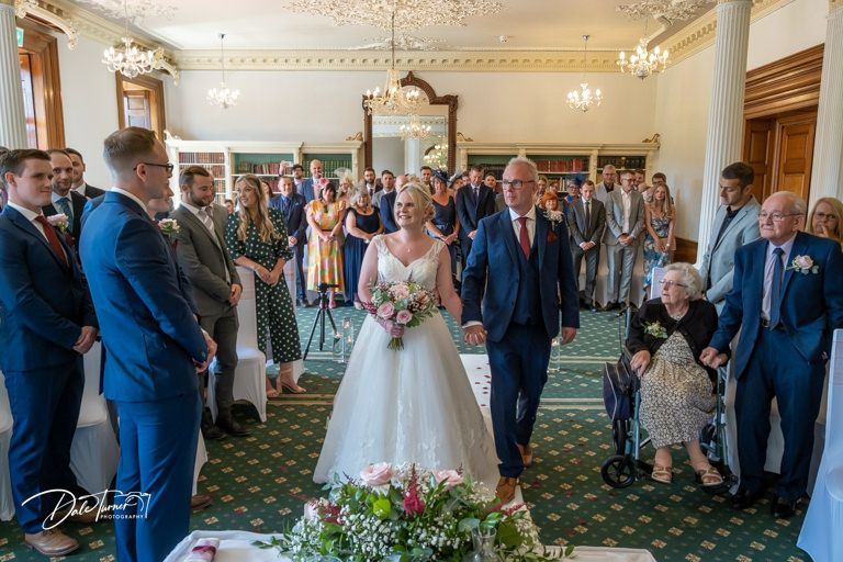 Panoramic view of wedding ceremony in grand room with green carpet and chandeliers.