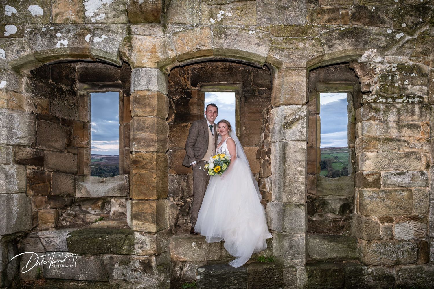 Wedding couple poses in rustic stone archways of ancient ruins during outdoor photo session.