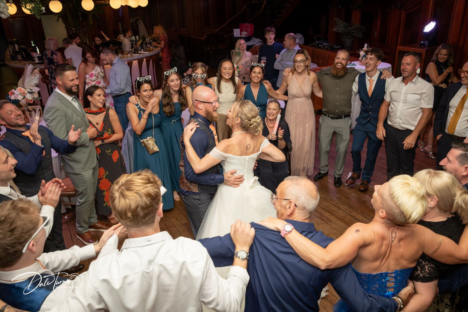 Bride and groom share first dance surrounded by wedding guests in teal bridesmaid dresses at elegant reception.
