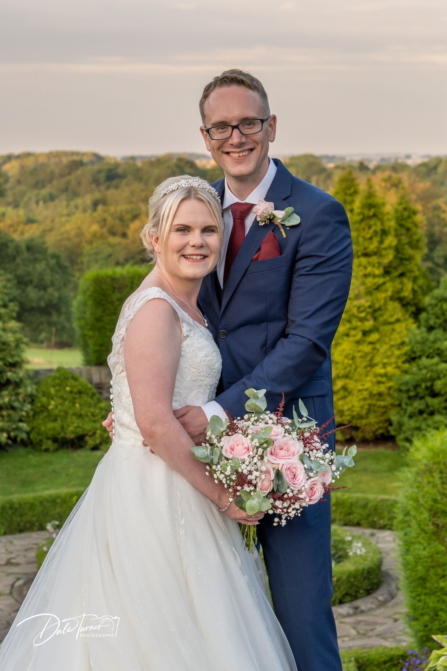 Newlyweds share intimate moments in a scenic hilltop garden setting.