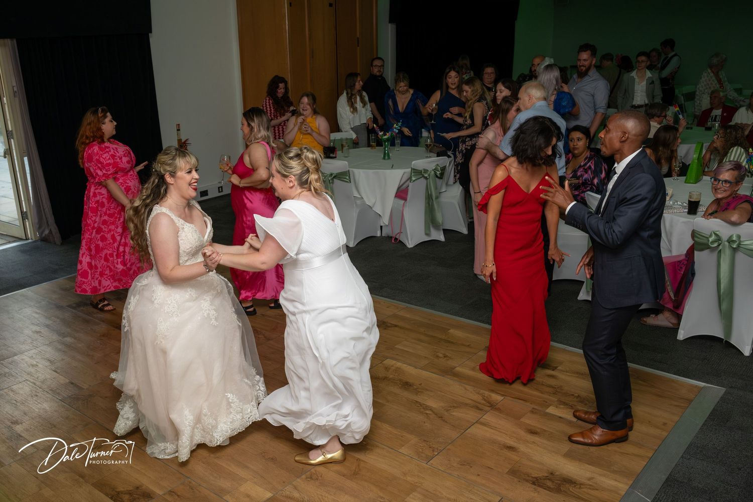 Wedding reception dance floor with guests in colorful attire enjoying the celebration.
