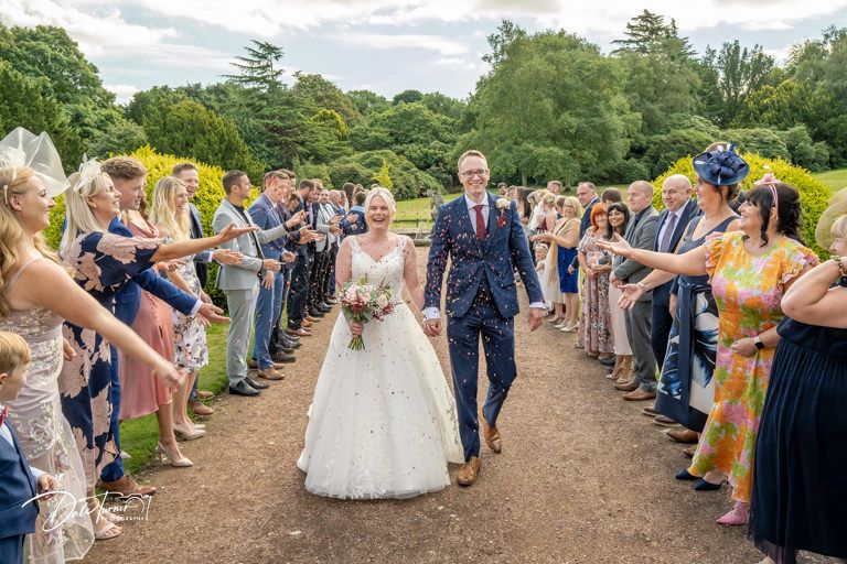 Wedding guests form two rows creating an aisle path outdoors for the wedding couple.