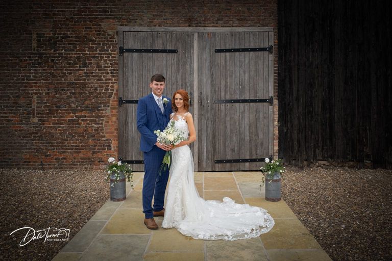 Wedding party poses against rustic brick wall and wooden barn door backdrop.