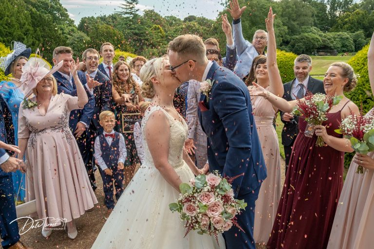 Wedding guests form a celebratory line outdoors as newlyweds walk through.