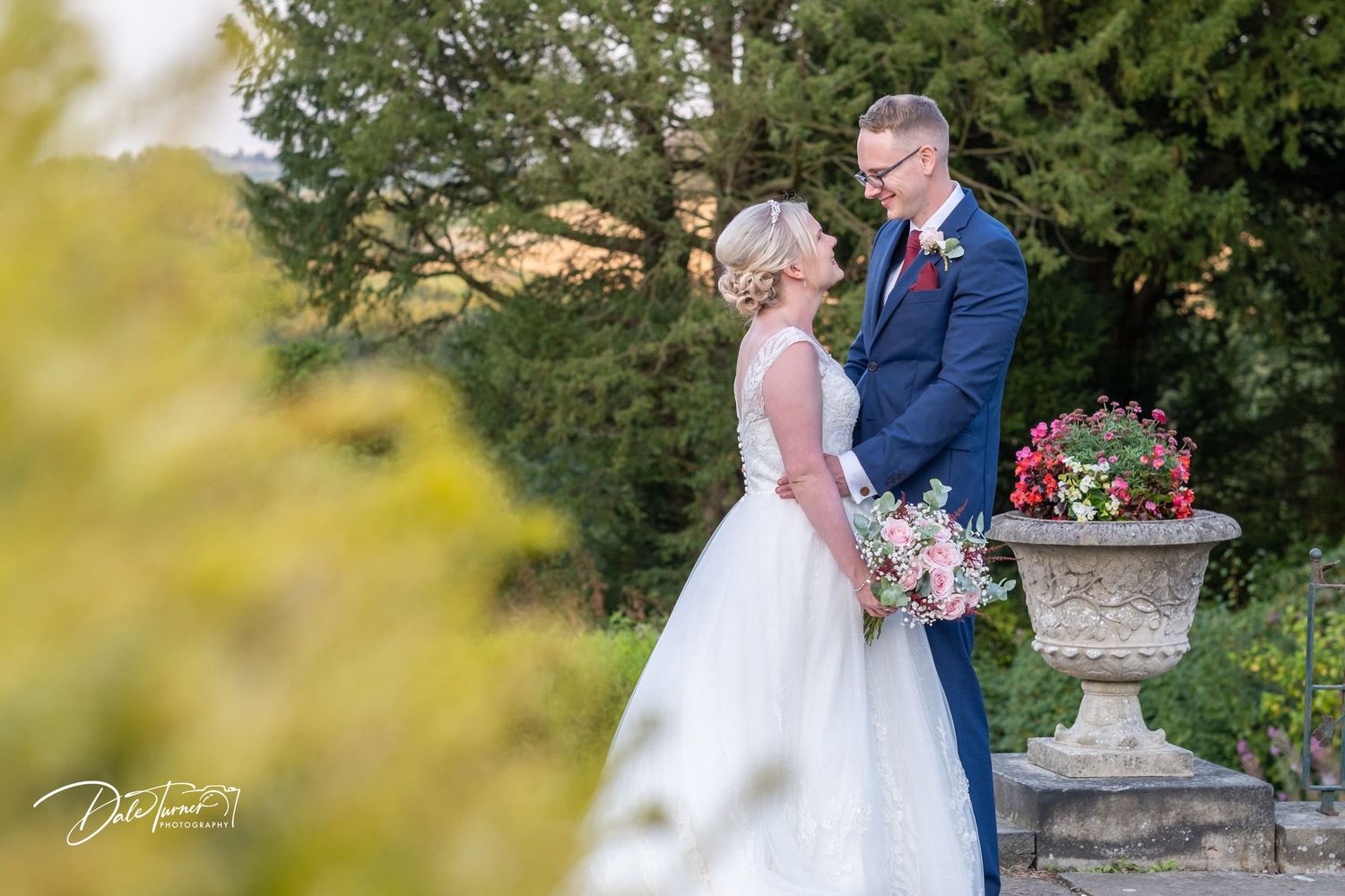 Romantic garden wedding portraits with ornate stone urns and colorful flowers.