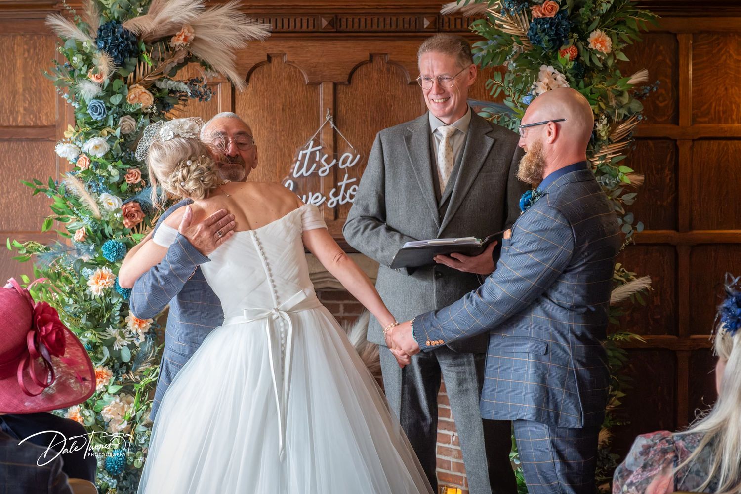 Bride and groom exchange vows at floral altar with officiant, in elegant wedding ceremony indoor setting.