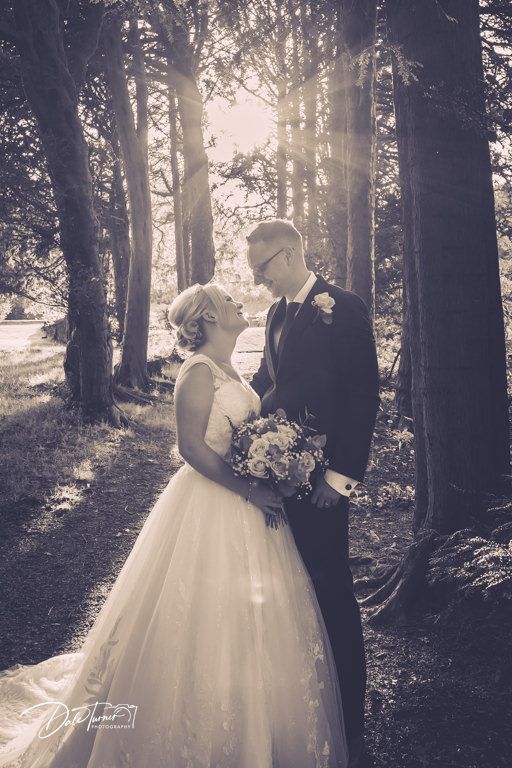 Romantic black and white wedding photo with sunlight streaming through trees.