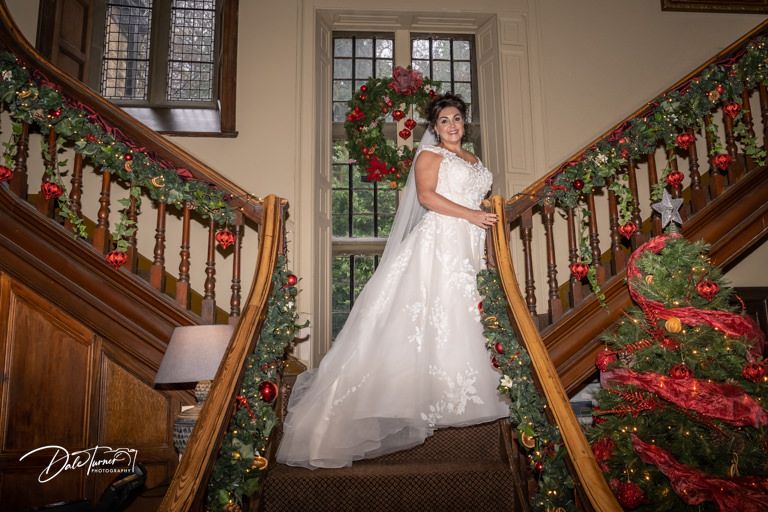 Bridal portrait on wooden staircase decorated with Christmas garland and red ornaments.