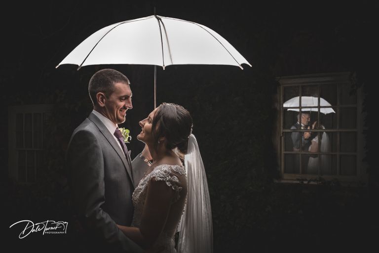 A couple shares an intimate moment under a white umbrella during their wedding photoshoot.
