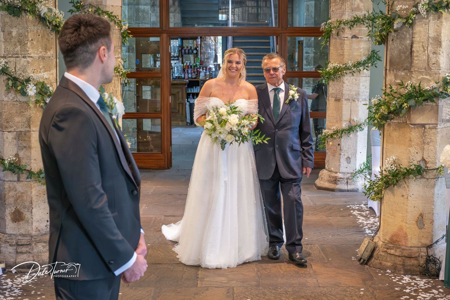 Wedding party stands beneath stone archway entrance during ceremony.